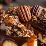 Slice of Turtle Fudge Cheesecake with chocolate drizzle and nuts