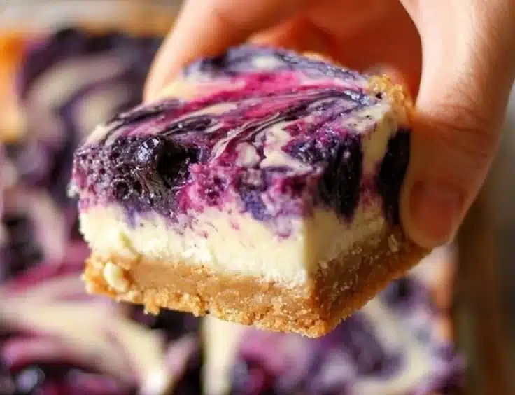 Blueberry Cheesecake Bars Recipe (Homemade) 3 Delicious homemade blueberry cheesecake bars on a white plate.
